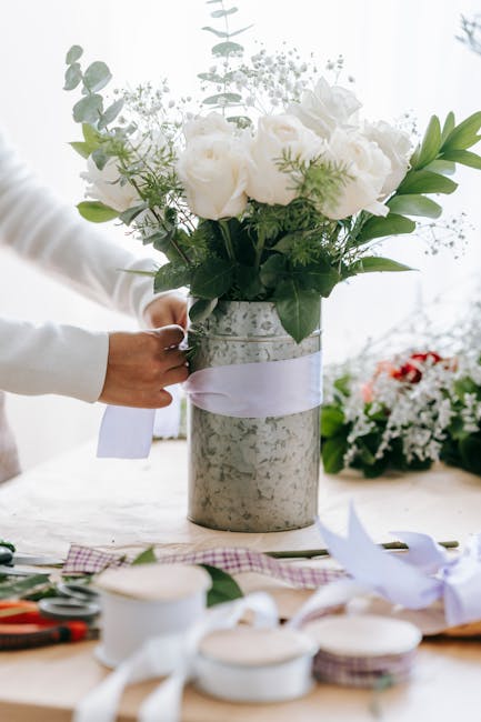 A bride and groom hold a vibrant floral bouquet featuring a mix of orange, red, pink, and white flowers, including roses, protea, and calla lilies, accented with dusty miller and eucalyptus foliage. T