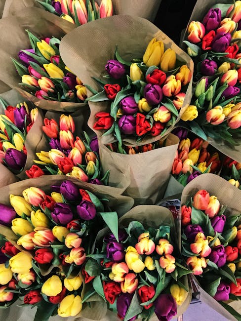 A diverse display of fresh flower bouquets arranged outdoors on a wooden stand, featuring a vibrant array of colours including pink, red, orange, white, yellow, and purple. The arrangements include ro